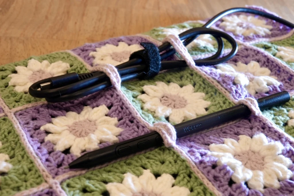 Close up of a bundled USB C cable and a tablet pen attached to a crocheted tablet sleeve with 4 simple strips of single crochets along the border lines in pink